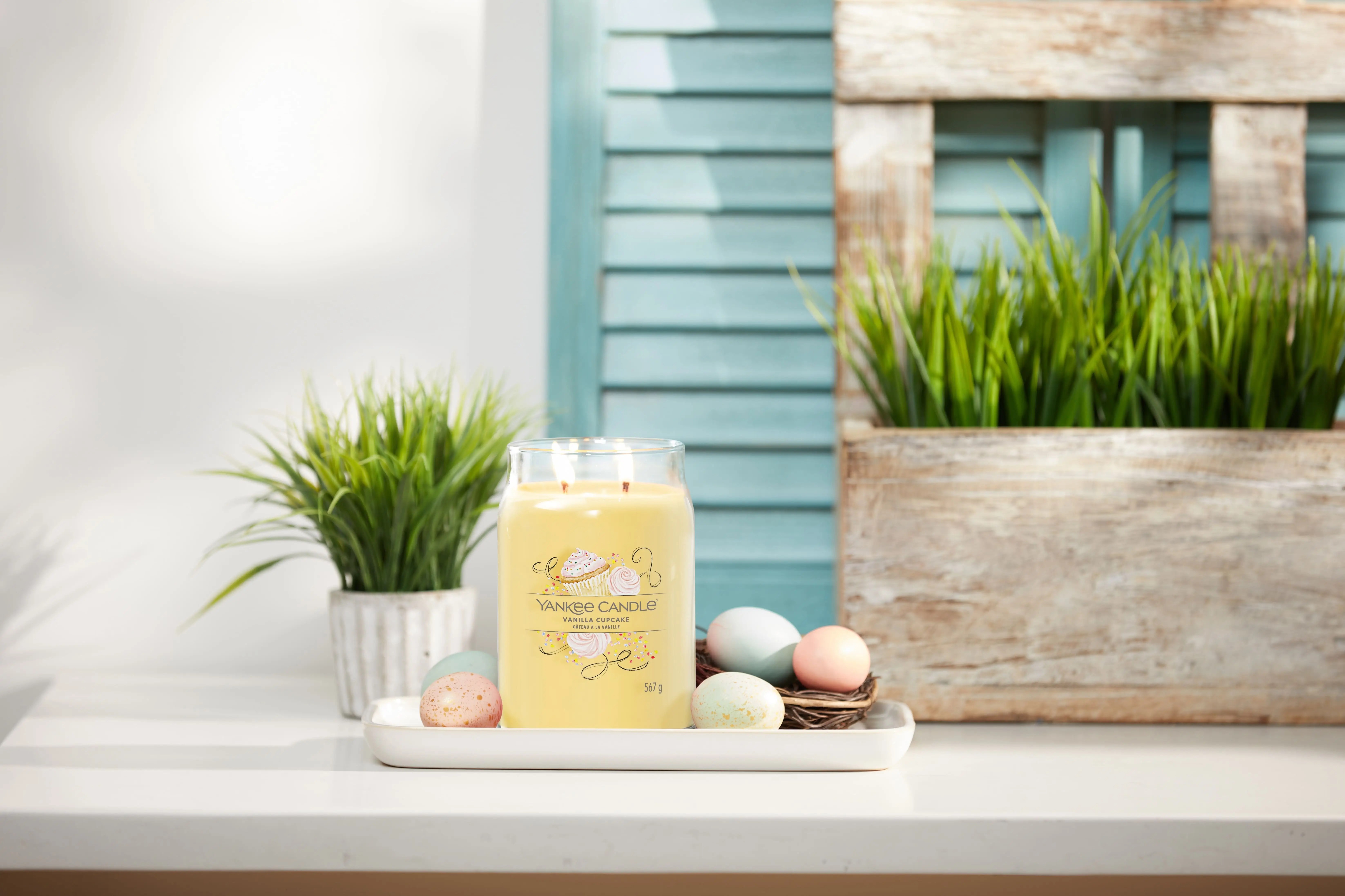 Candela Vanilla Cupcake di Yankee Candle® accesa, circondata da ovetti pasquali e decorazioni primaverili, atmosfera calda e dolce